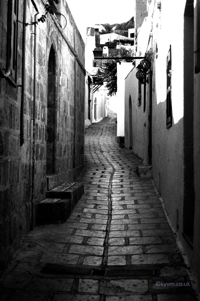 Lindos is known for its fortified Acropolis perched atop a natural rock formation, surrounded by a sprawling tightly packed town of narrow streets and alleyways.  Over many years of use the cobbles and flagstones have been polished smooth and great care is needed not to fall.